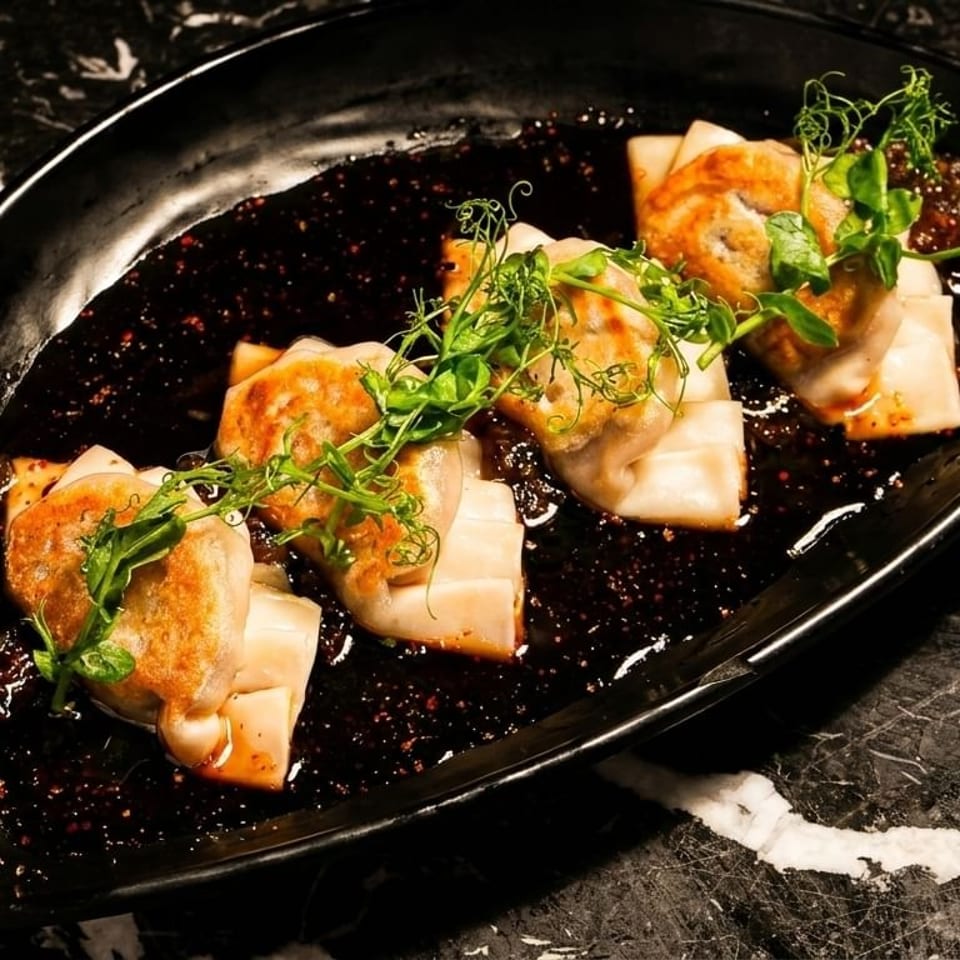 Pan-fried dumplings with a dark sauce and green garnish on a black plate.