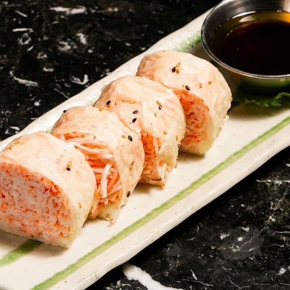 Four pieces of sushi with crab meat and white fish, served with soy sauce on a white plate.