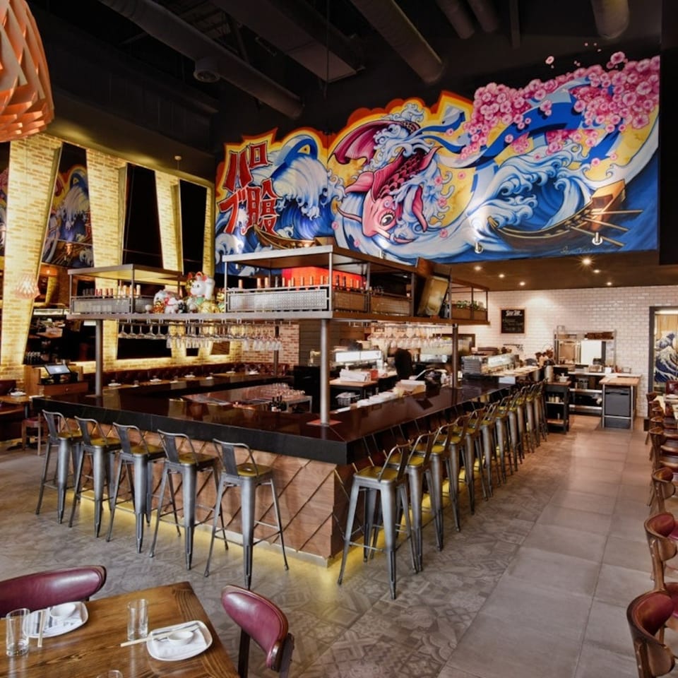 Spacious restaurant interior with a long bar, dining tables, and a large Japanese-style mural.